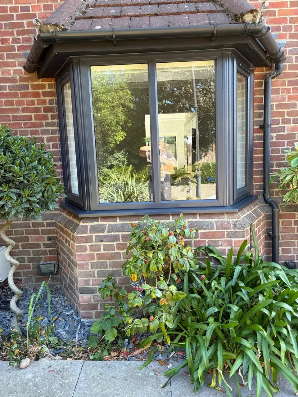 Dark grey bay window fitted to a brick home with garden outlook