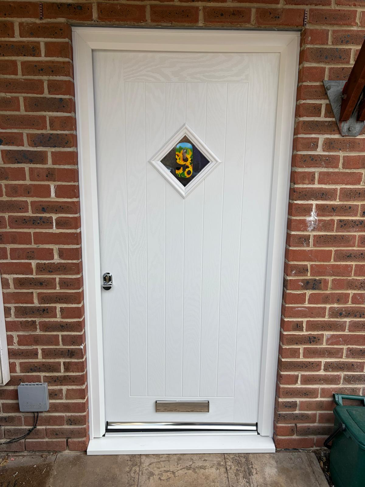 White composite front door with diamond glazing installed in a red brick home