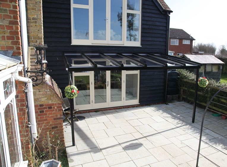Contemporary black aluminium and glass canopy over French doors opening onto a paved patio