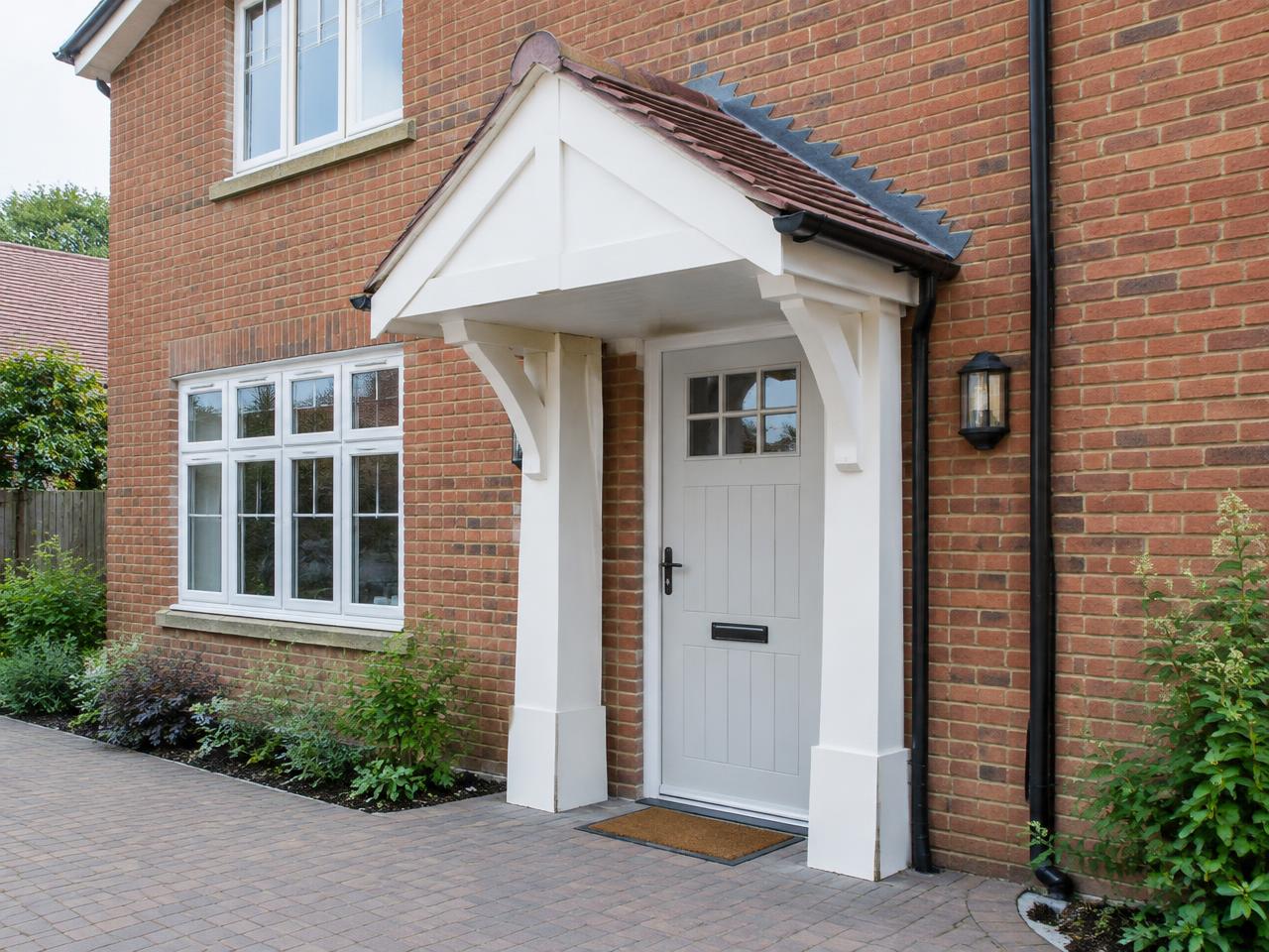 Classic white pitched door canopy with a tiled apex roof on a detached brick house
