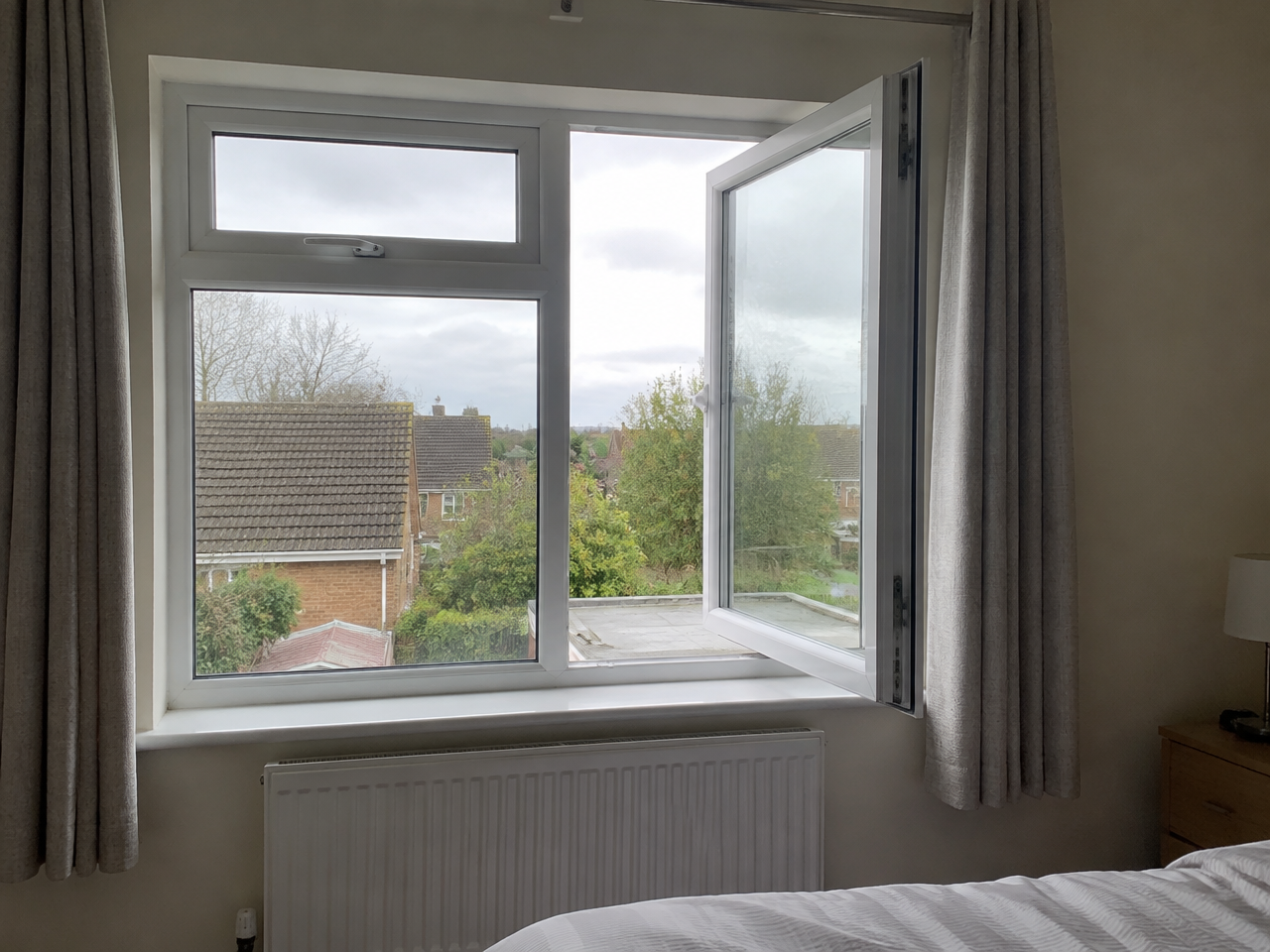 White side-hung casement window opening outwards in a bedroom