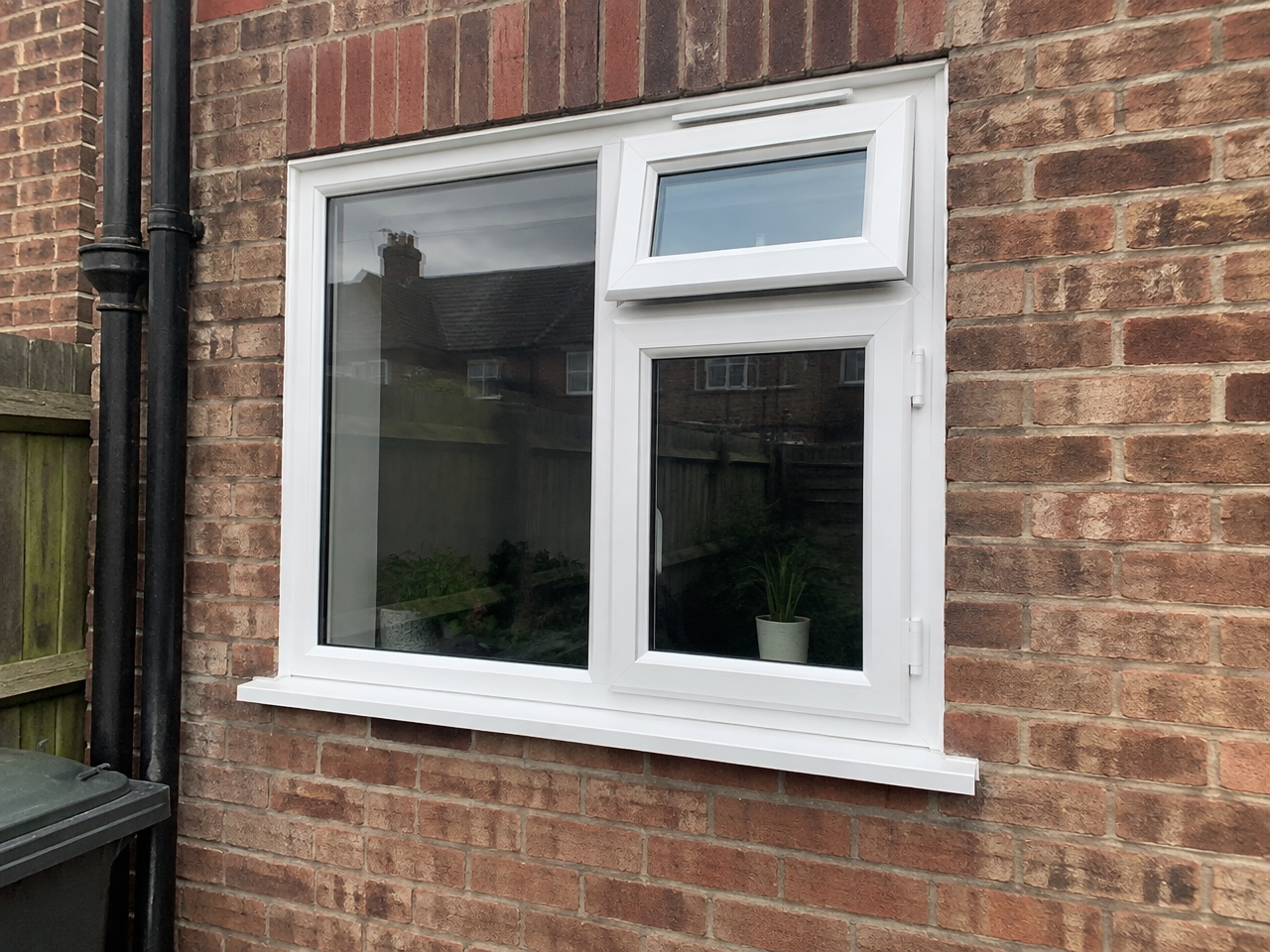 White casement window with an outward-opening top section in a brick wall