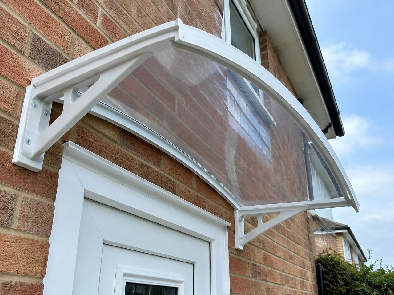 Underside view of a curved white door canopy with clear glazing and support brackets